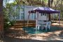 Casetta con gazebo viola e tavolo da esterno in una zona alberata.